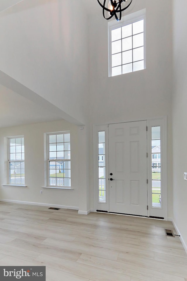 entrance foyer with a high ceiling, light wood finished floors, visible vents, baseboards, and a notable chandelier