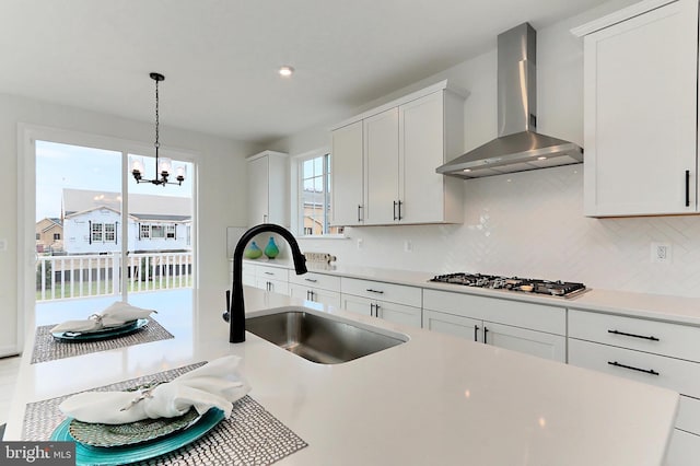 kitchen with wall chimney exhaust hood, stainless steel gas cooktop, a sink, backsplash, and light countertops