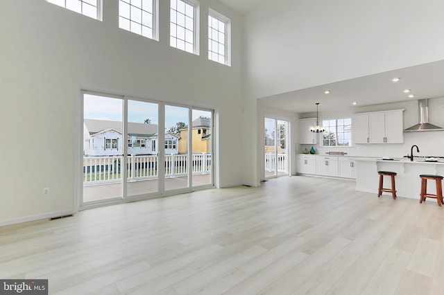 unfurnished living room with a chandelier, light wood-style flooring, a high ceiling, and a sink