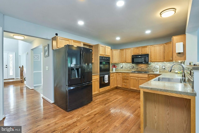 kitchen featuring a sink, light wood finished floors, black appliances, and decorative backsplash