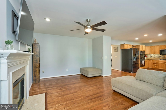 living area with a ceiling fan, a fireplace with flush hearth, wood finished floors, baseboards, and recessed lighting