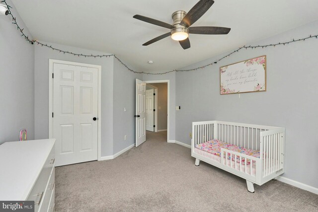 bedroom with a crib, baseboards, light carpet, and a ceiling fan