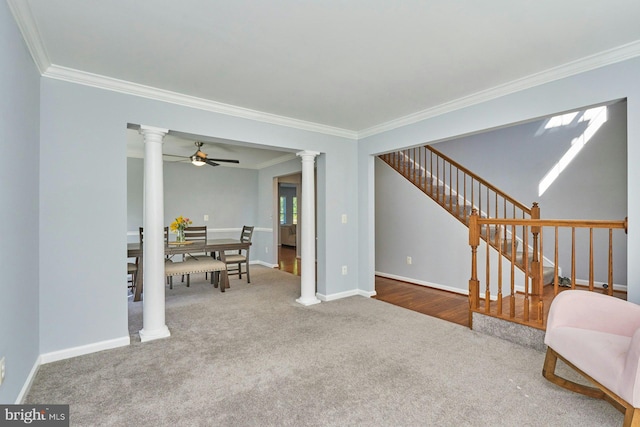 carpeted living room with crown molding, ceiling fan, stairs, baseboards, and ornate columns