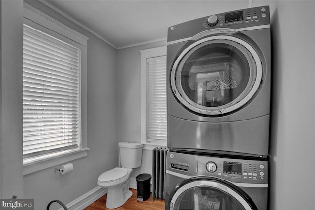 laundry area featuring crown molding, stacked washer and dryer, laundry area, radiator, and wood finished floors