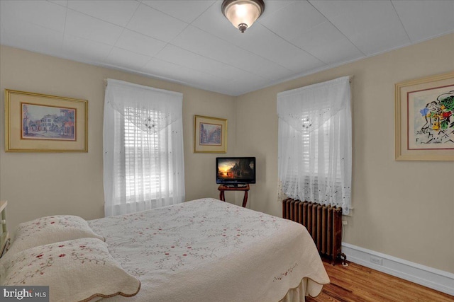 bedroom featuring wood finished floors, baseboards, and radiator heating unit