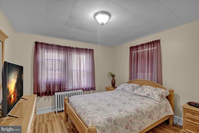bedroom with baseboards, radiator, and light wood-style floors