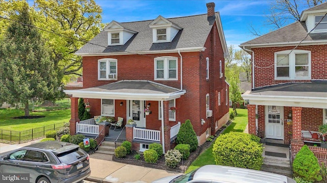 view of front of house with fence, a shingled roof, brick siding, a chimney, and covered porch