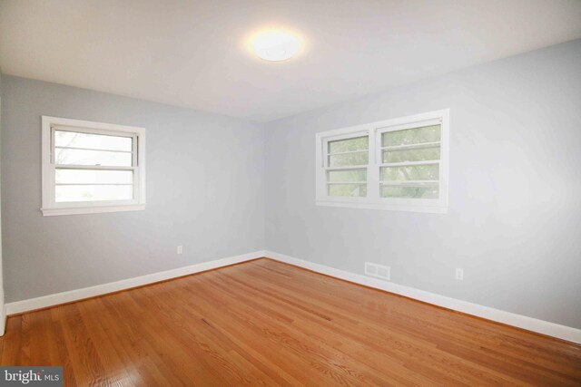 unfurnished room with healthy amount of natural light, wood finished floors, and baseboards
