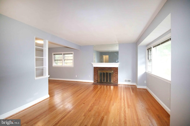 unfurnished living room with light wood-style flooring, a brick fireplace, and baseboards