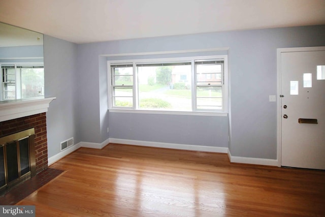 unfurnished living room with wood finished floors, baseboards, and a brick fireplace