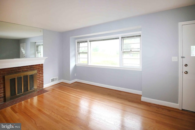 unfurnished living room featuring wood finished floors, baseboards, and a brick fireplace