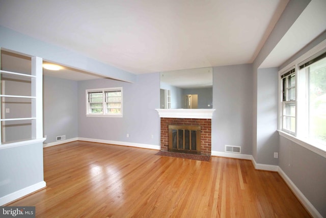 unfurnished living room with light wood-style floors, a brick fireplace, and baseboards