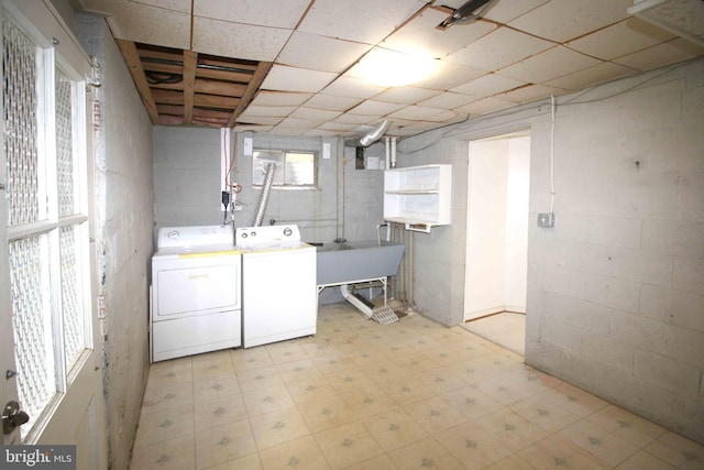 clothes washing area featuring washer and dryer, light flooring, a sink, and concrete block wall