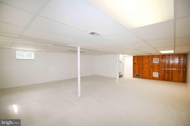 below grade area with a paneled ceiling, wooden walls, carpet flooring, and stairway
