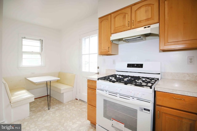 kitchen featuring white gas stove, under cabinet range hood, light countertops, and plenty of natural light