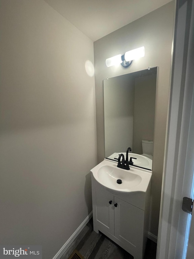 bathroom featuring baseboards, wood finished floors, vanity, and toilet