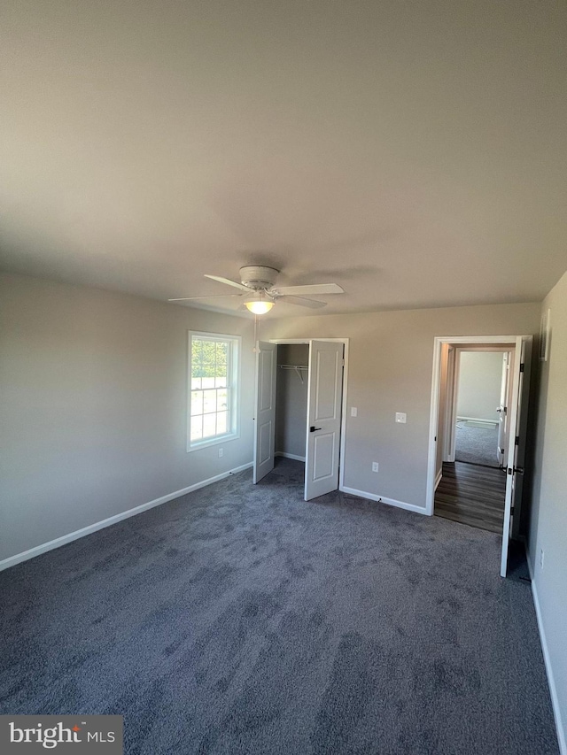 unfurnished bedroom with dark colored carpet, a closet, baseboards, and ceiling fan