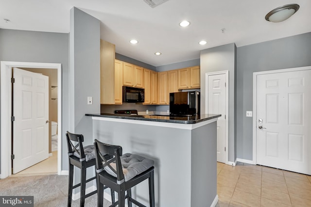 kitchen featuring a breakfast bar area, light brown cabinetry, dark countertops, and black appliances