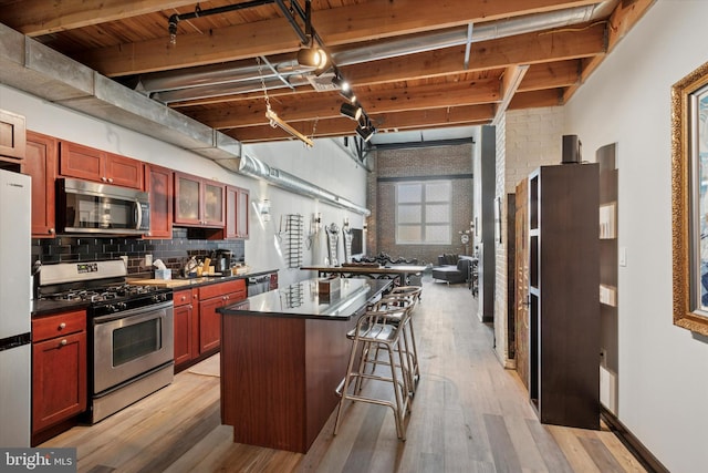 810 N Hancock St Unit 5, Philadelphia, PA 19123 - kitchen featuring a kitchen island, dark countertops, beamed ceiling, reddish brown cabinets, and stainless steel appliances