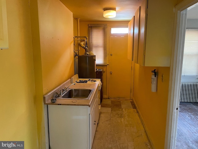 kitchen featuring gas water heater, radiator heating unit, a sink, and white cabinetry