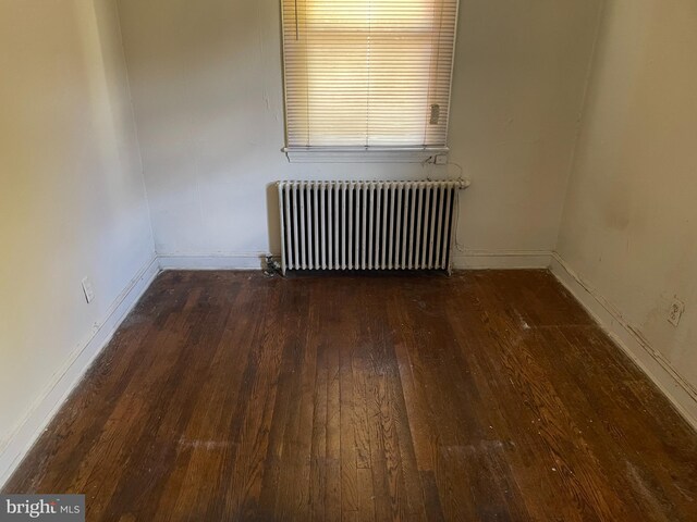 unfurnished room featuring wood-type flooring, baseboards, and radiator