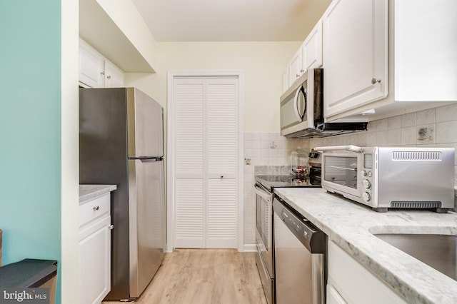 kitchen featuring light wood finished floors, a toaster, stainless steel appliances, decorative backsplash, and white cabinetry