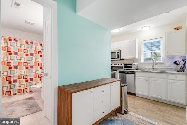kitchen with white cabinets, stainless steel appliances, a sink, tasteful backsplash, and visible vents