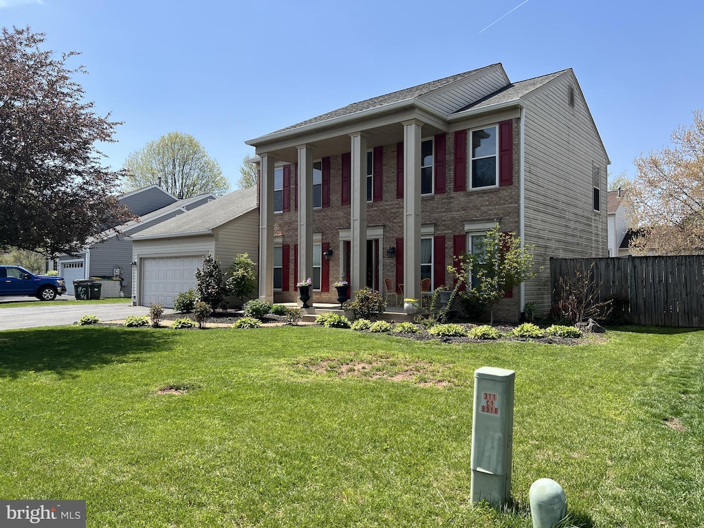 greek revival house with a front lawn, fence, brick siding, concrete driveway, and an attached garage