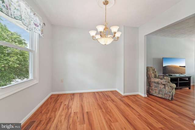 unfurnished dining area with a chandelier, wood finished floors, and baseboards