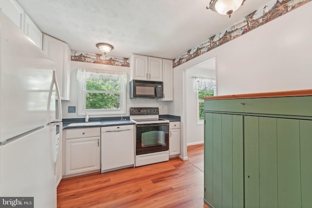kitchen with white appliances, a sink, white cabinetry, and healthy amount of natural light