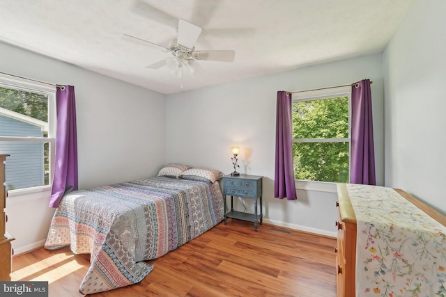 bedroom featuring wood finished floors, multiple windows, ceiling fan, and baseboards