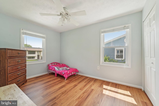 bedroom with light wood finished floors, multiple windows, baseboards, and a closet