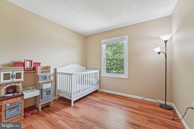 bedroom featuring light wood-style flooring, baseboards, a textured ceiling, and a crib