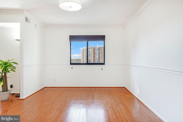 spare room with a textured ceiling, visible vents, baseboards, wood finished floors, and crown molding