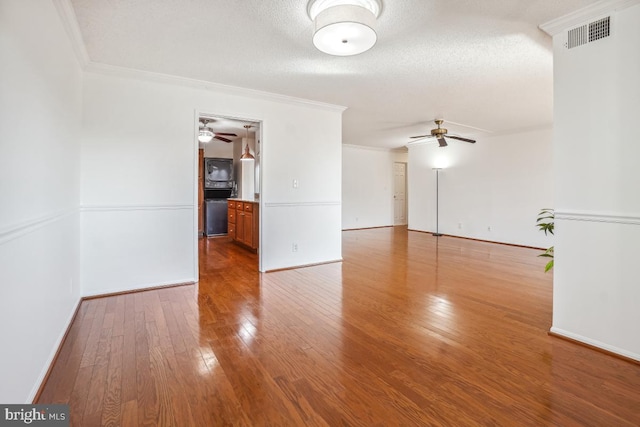empty room with wood finished floors, visible vents, a ceiling fan, and ornamental molding