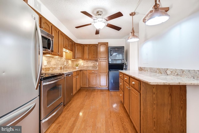 kitchen featuring stainless steel appliances, backsplash, light wood-style floors, a ceiling fan, and brown cabinets