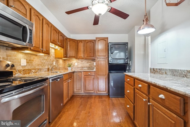 kitchen featuring stainless steel appliances, light wood-style flooring, a sink, a textured ceiling, and stacked washer / drying machine