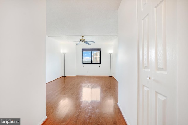 empty room featuring wood finished floors, a ceiling fan, and baseboards