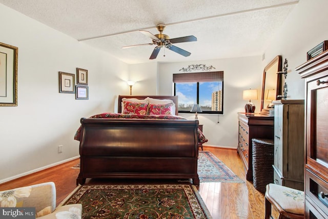 bedroom with wood finished floors, a textured ceiling, a ceiling fan, and baseboards