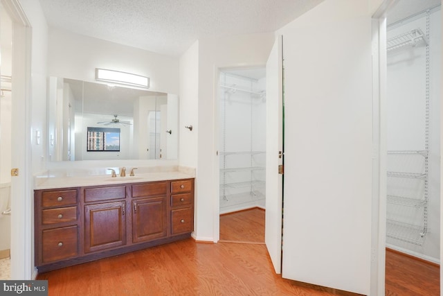 full bathroom with wood finished floors, a spacious closet, a ceiling fan, and vanity