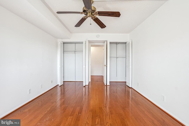 unfurnished bedroom with wood finished floors, a ceiling fan, baseboards, and two closets