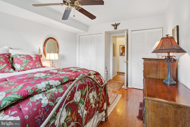 bedroom with hardwood / wood-style floors, two closets, and ceiling fan