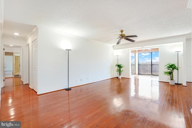 unfurnished living room featuring a textured ceiling, baseboards, wood finished floors, ceiling fan, and ornamental molding