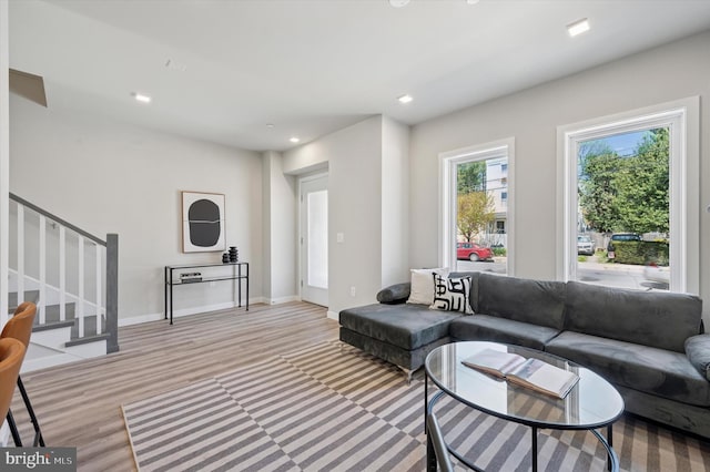 living room with light wood-type flooring, baseboards, recessed lighting, and stairway
