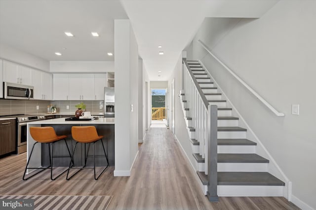 kitchen featuring stainless steel appliances, light wood-type flooring, white cabinetry, decorative backsplash, and light countertops