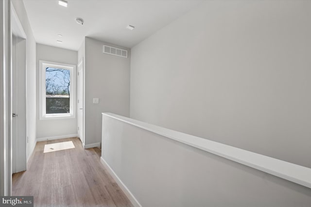 hall with baseboards, light wood-style flooring, visible vents, and an upstairs landing