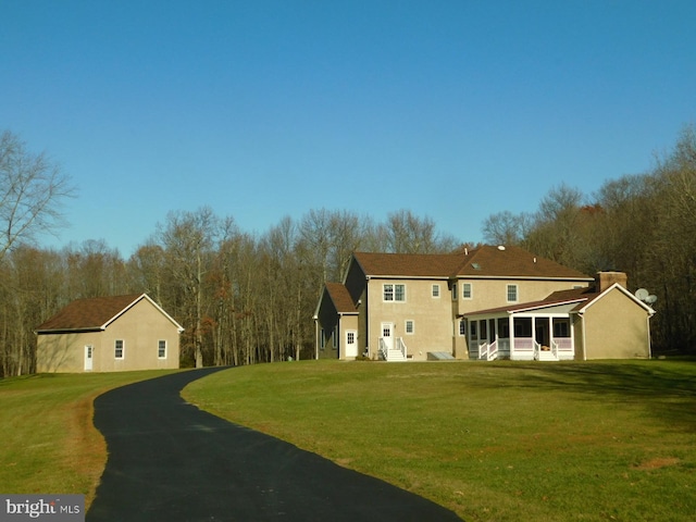 back of property with a lawn, a sunroom, and stucco siding
