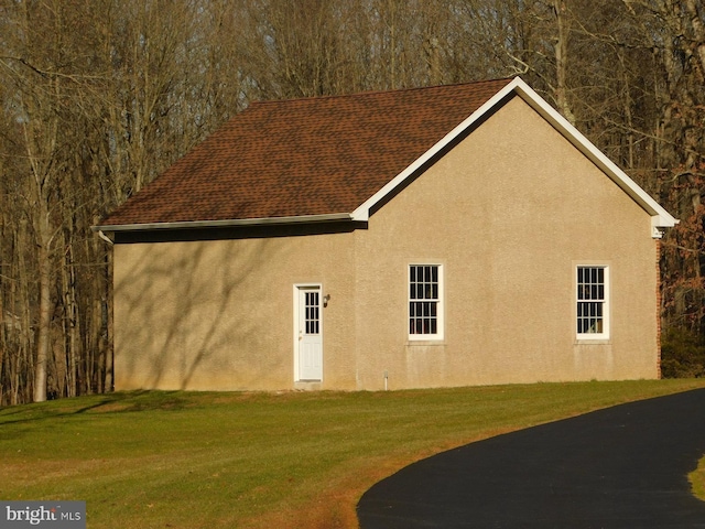 view of side of property with a lawn, a shingled roof, and stucco siding