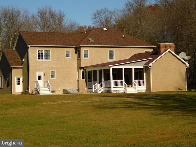 back of property with stucco siding, a sunroom, and a yard