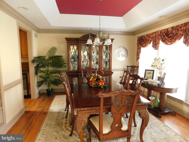 dining space with baseboards, visible vents, an inviting chandelier, hardwood / wood-style floors, and a raised ceiling